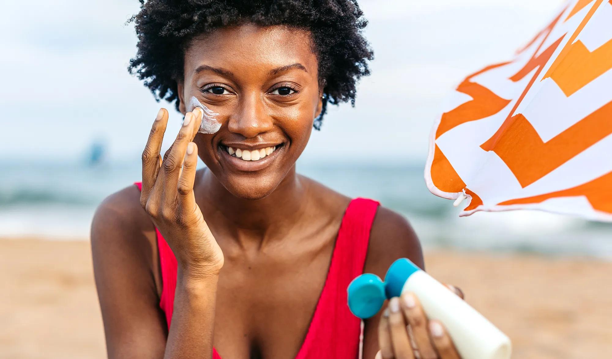Woman applying white sunscreen cream to her cheek at the beach