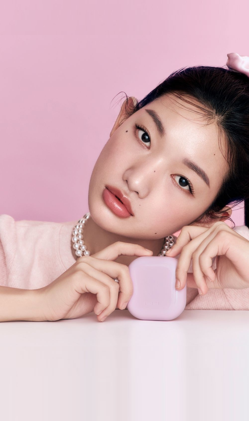 Model holding pink cushion compact beside smooth finished skin