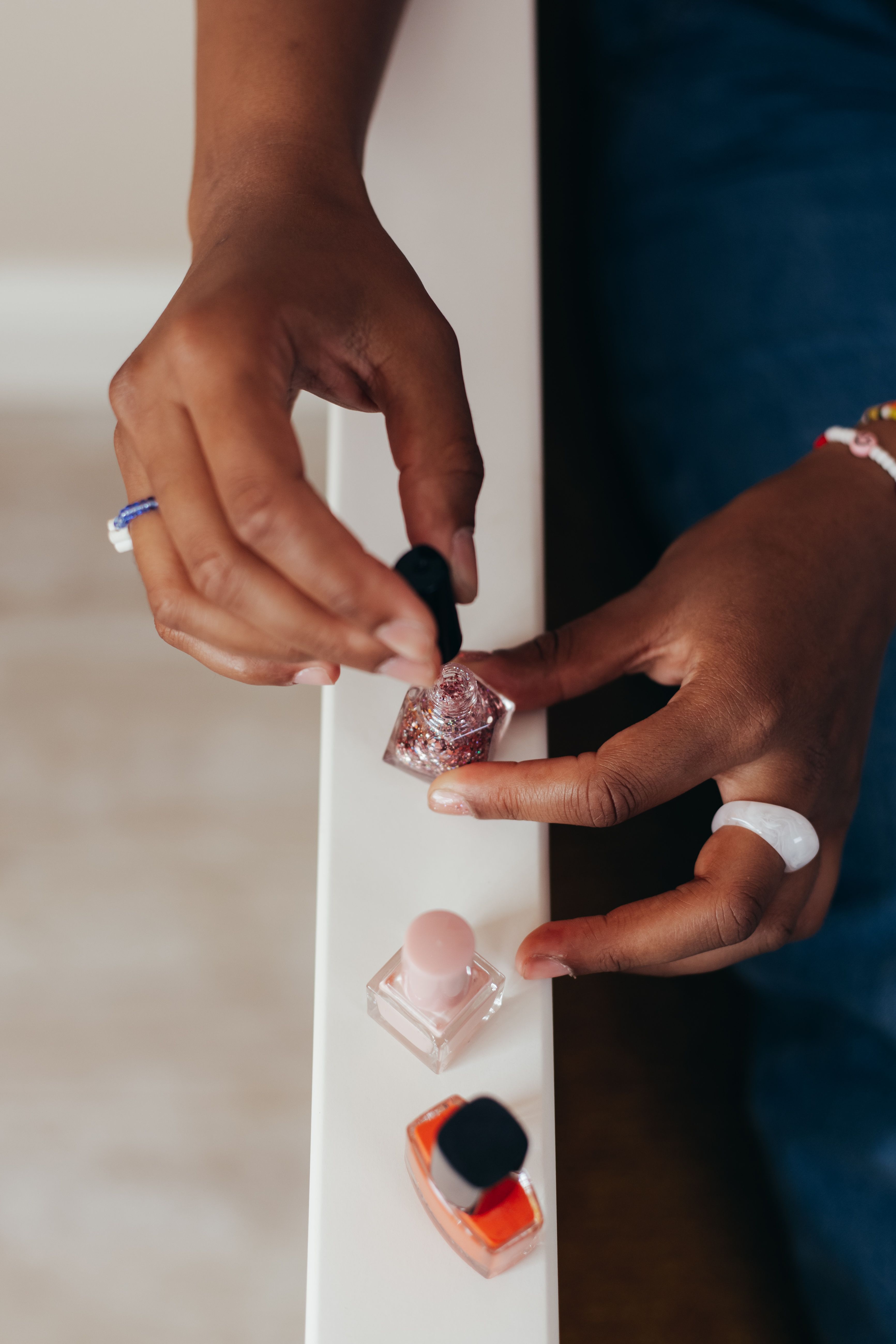 Hands holding an open glitter nail polish bottle beside colored lacquers
