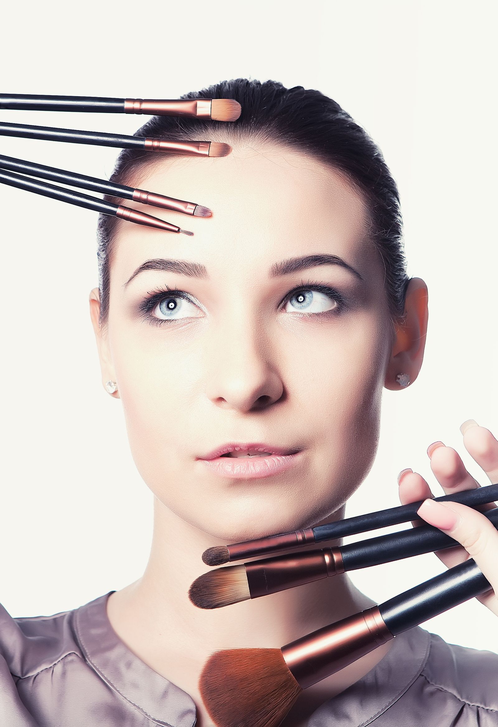 A woman poses with assorted makeup brushes held around her face