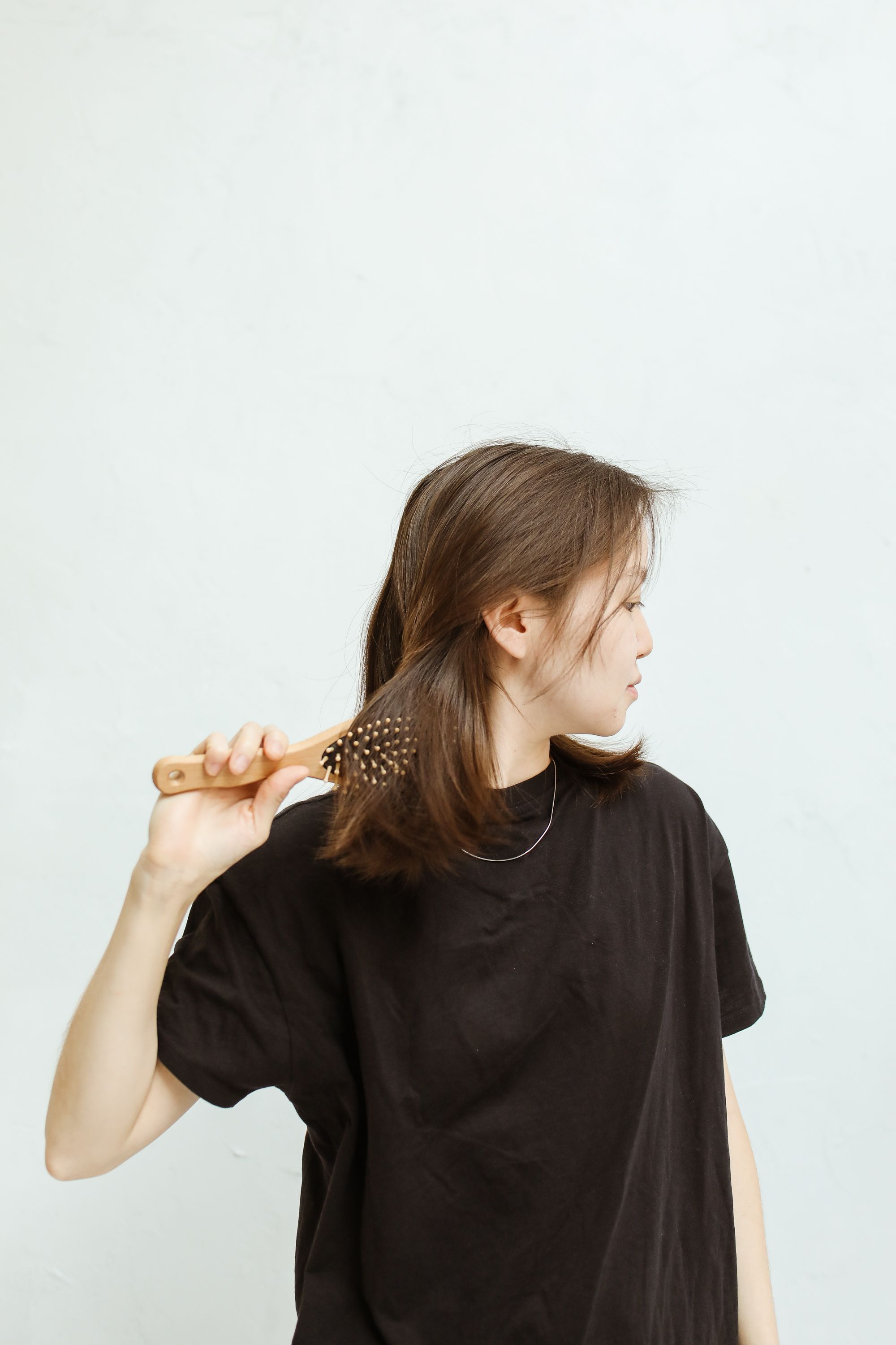 Woman brushing the lengths of her brown hair with a wooden paddle brush