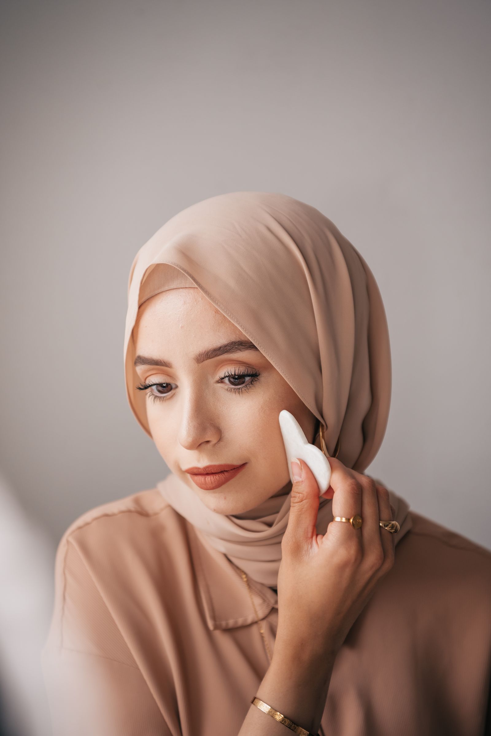 A woman in a beige headscarf holds a white applicator against her cheek