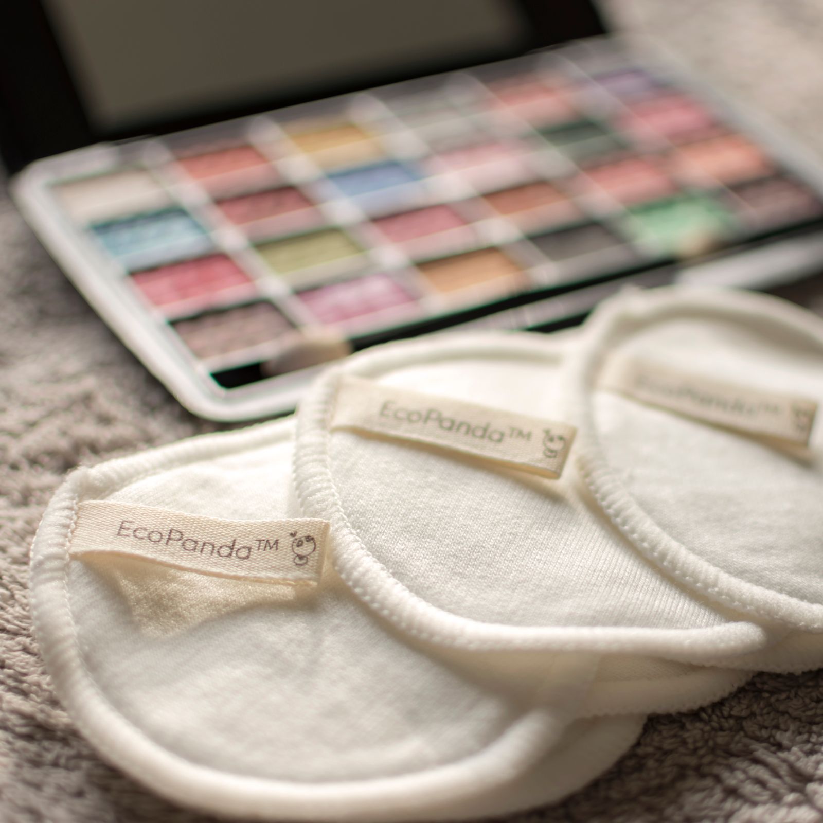 Stitched reusable EcoPanda makeup-remover rounds lie beside a colorful cosmetic palette